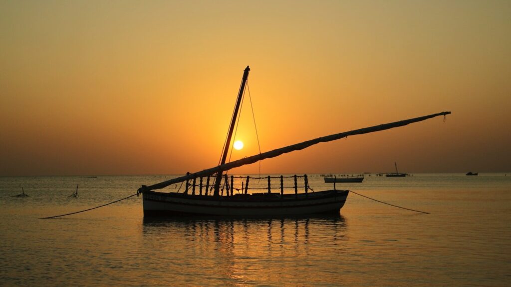 Sailboat silhouetted against a warm sunset over the ocean.